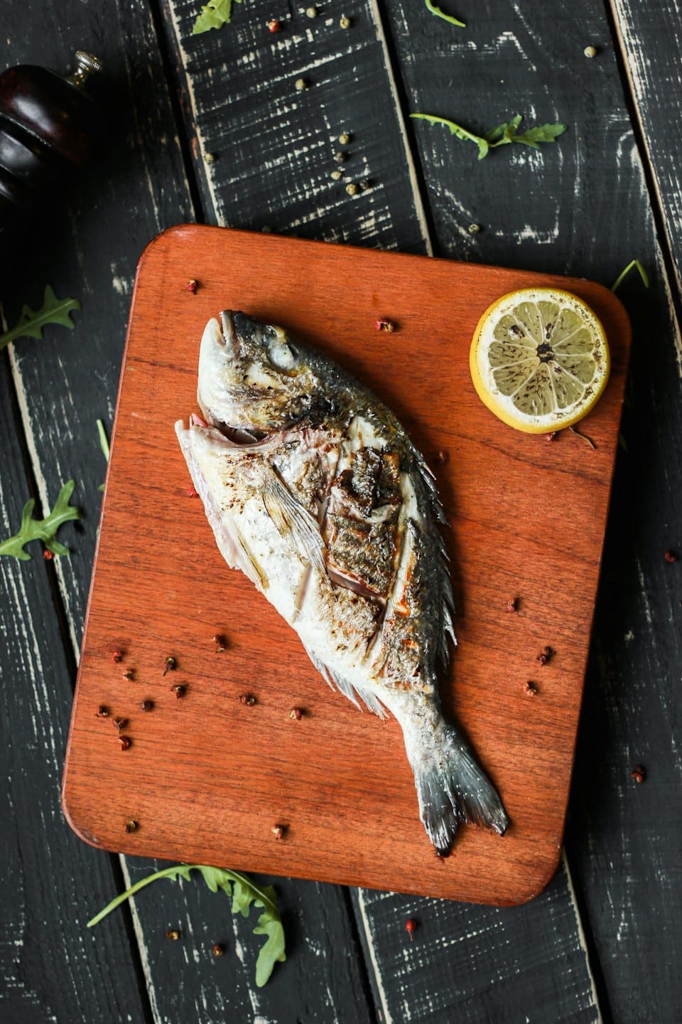 Pescado entero a la parrilla servido en una tabla de cortar de madera.