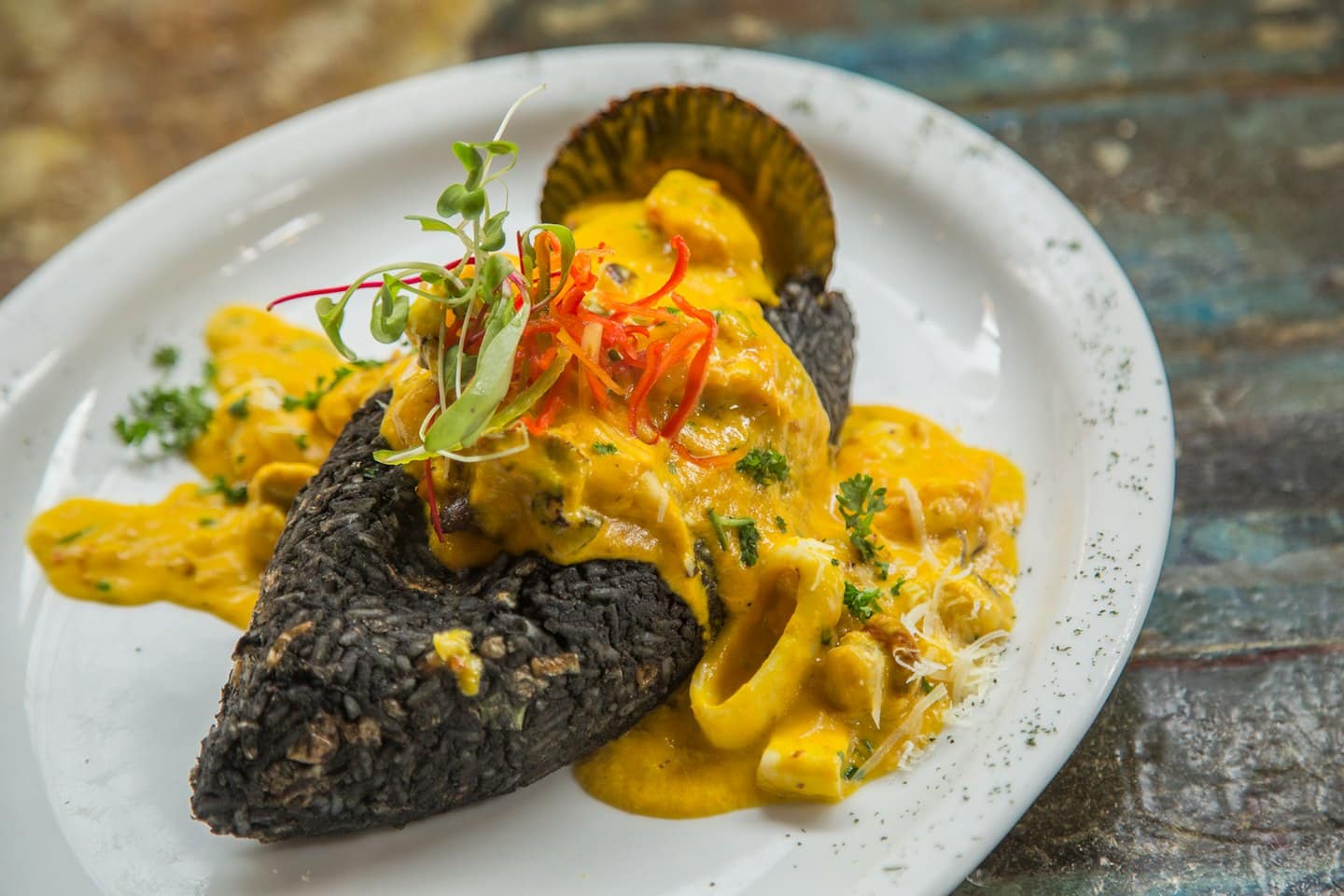 Pasta con mariscos, aros de calamar y microgreens en plato blanco.