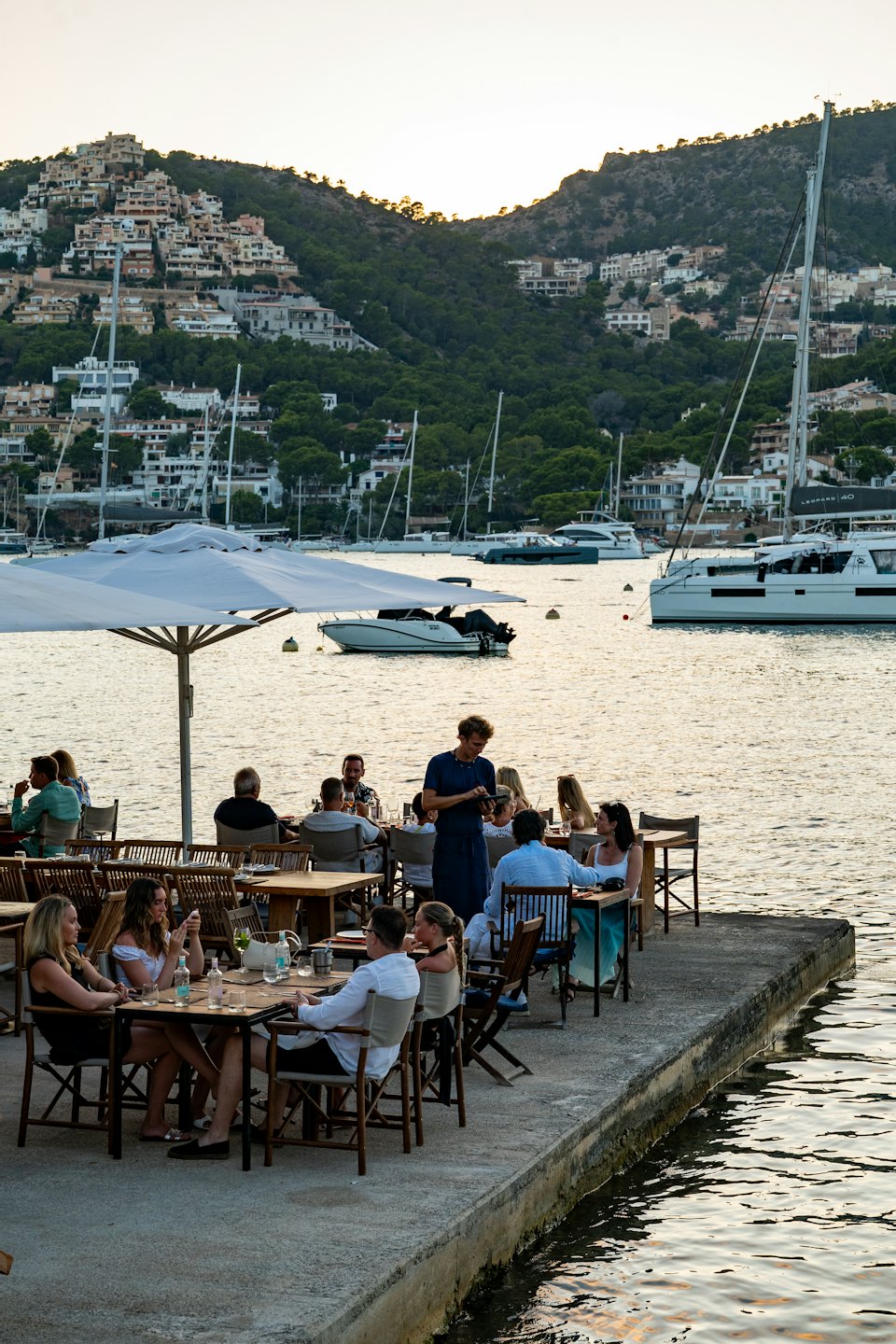 Gente cenando en un restaurante frente al mar mientras un camarero toma nota.