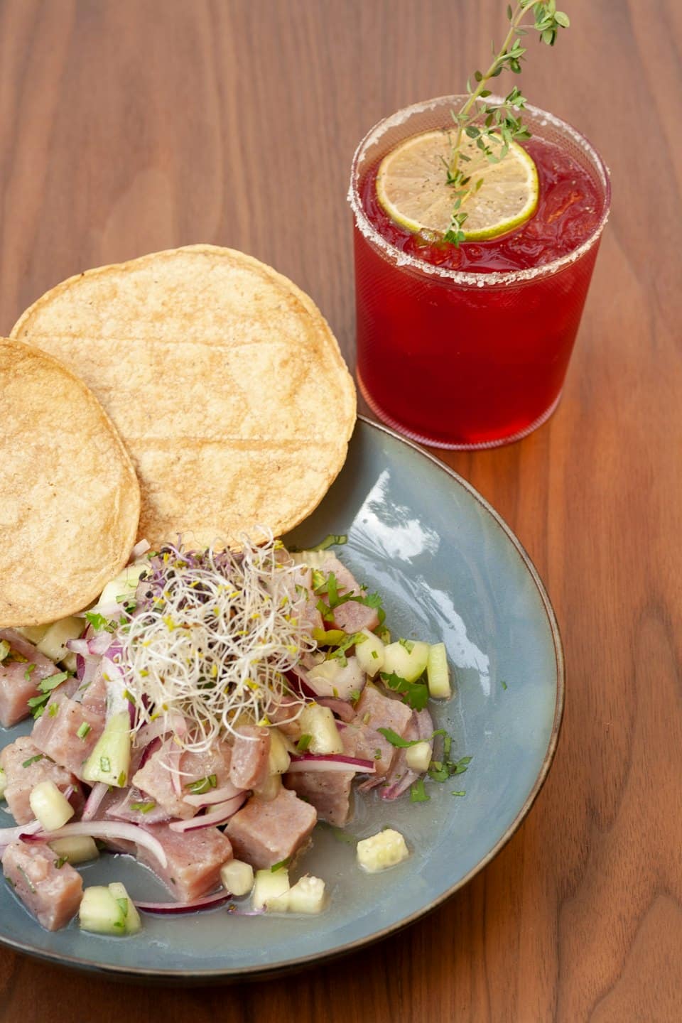 Ceviche fresco con tortillas de maíz y una bebida con lima sobre madera.