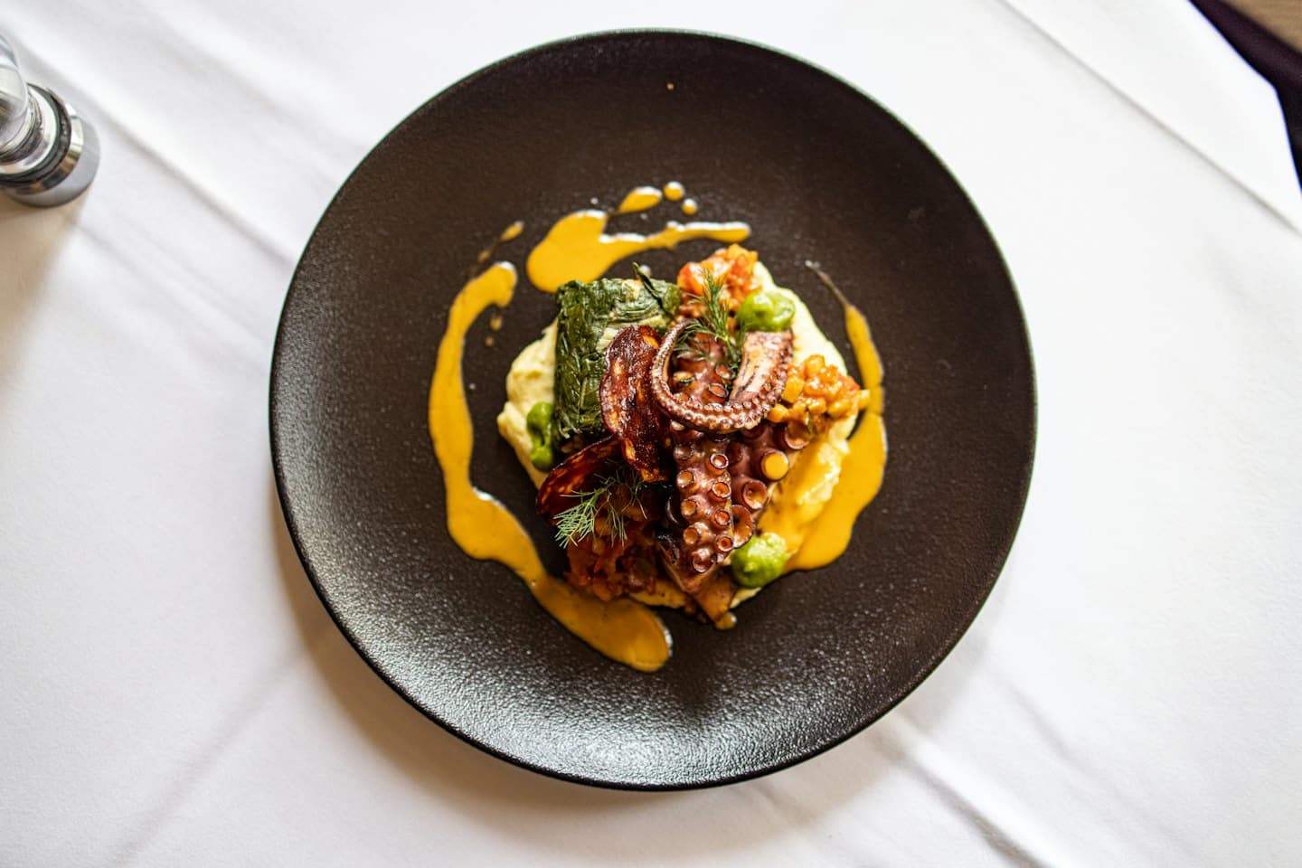 Tentáculos de pulpo a la parrilla con puré de patatas y verduras en un plato oscuro.